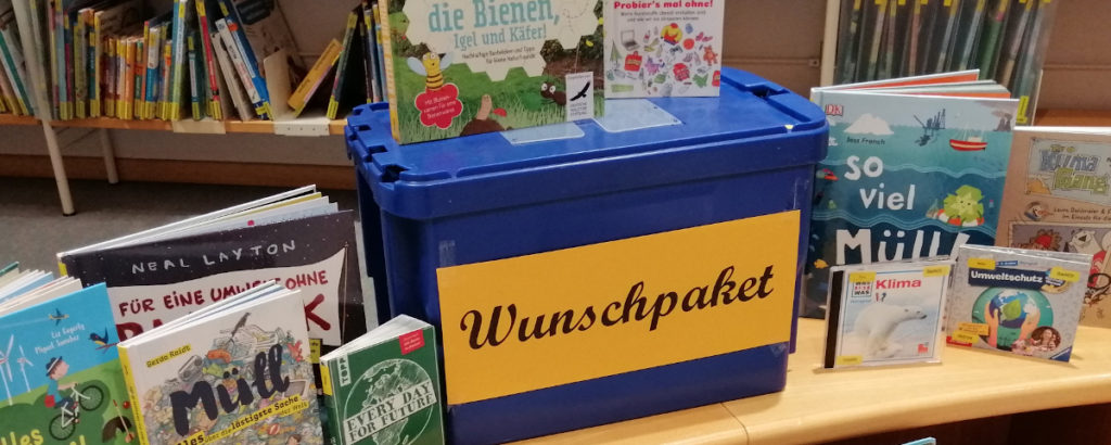 Blaue Kiste mit der Aufschrift Wunschpaket, darum Bücher und CDs zum Thema Müll
